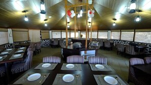 Um restaurante com cabines e mesas, teto de madeira e luminárias pendentes.