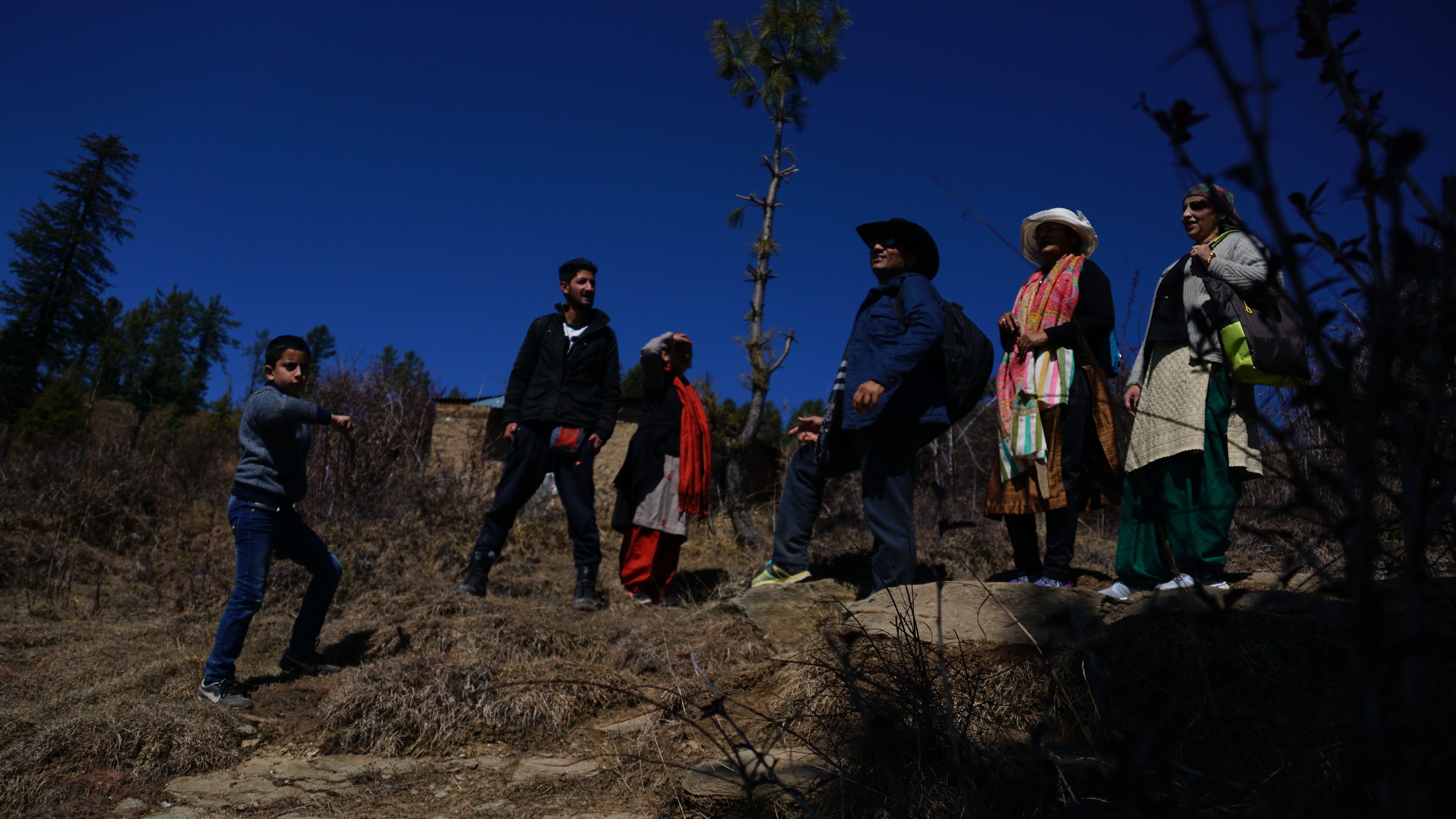 Un gruppo di persone in piedi su un terreno roccioso, con vegetazione rada e cielo azzurro intenso.