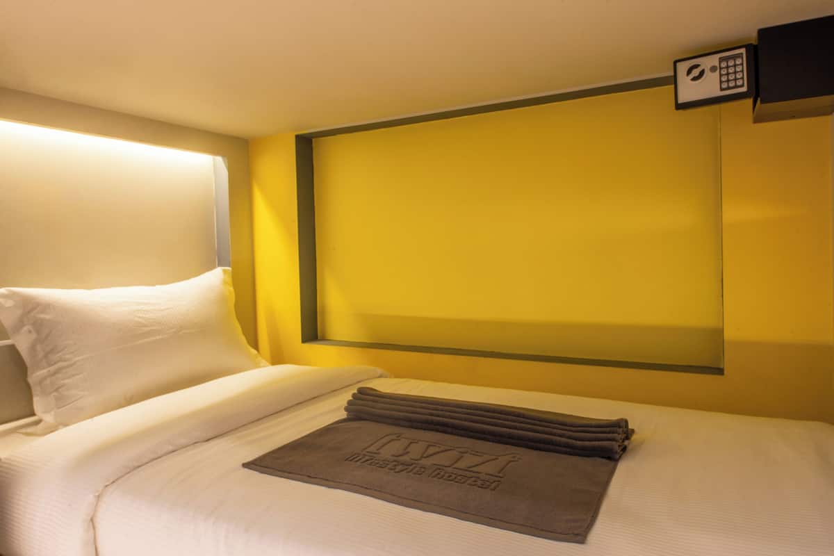 Une chambre d’hôtel avec un lit, des oreillers, une serviette pliée et un panneau de commande fixé au mur.