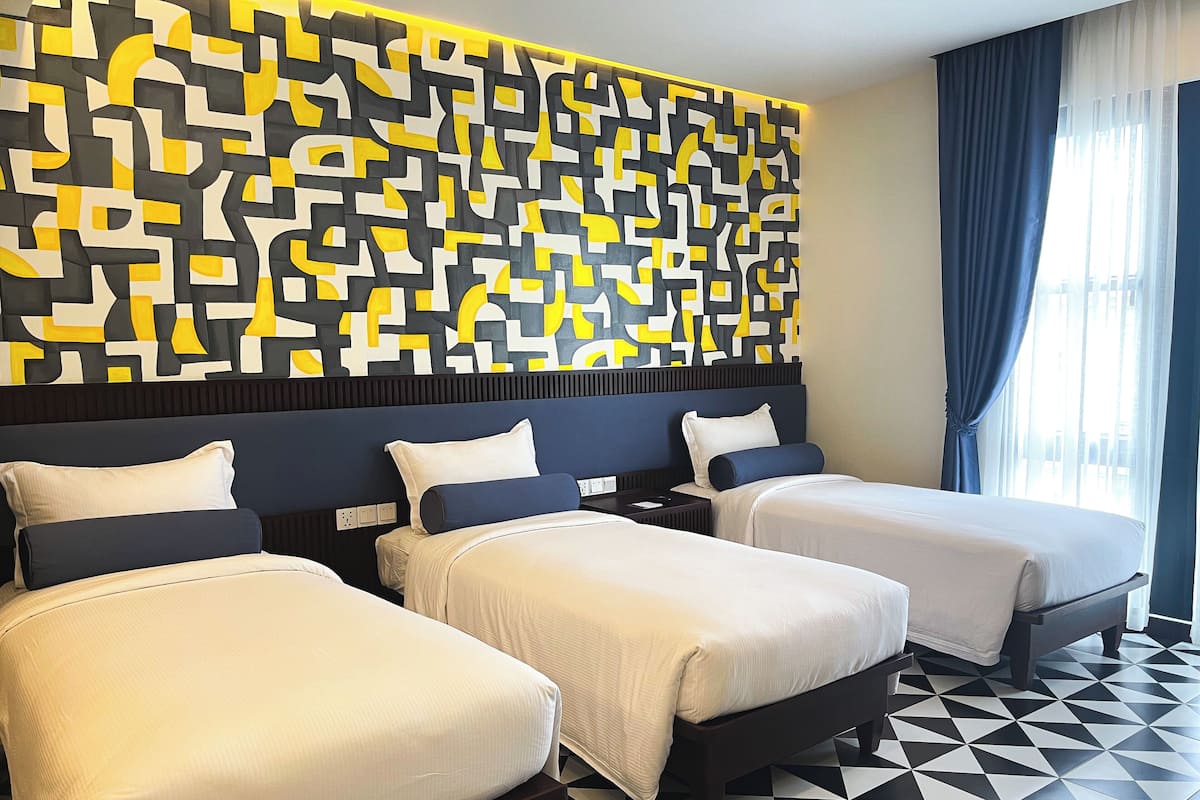 Une chambre d’hôtel avec trois lits, un mur orné d’un motif géométrique et un sol à carreaux.