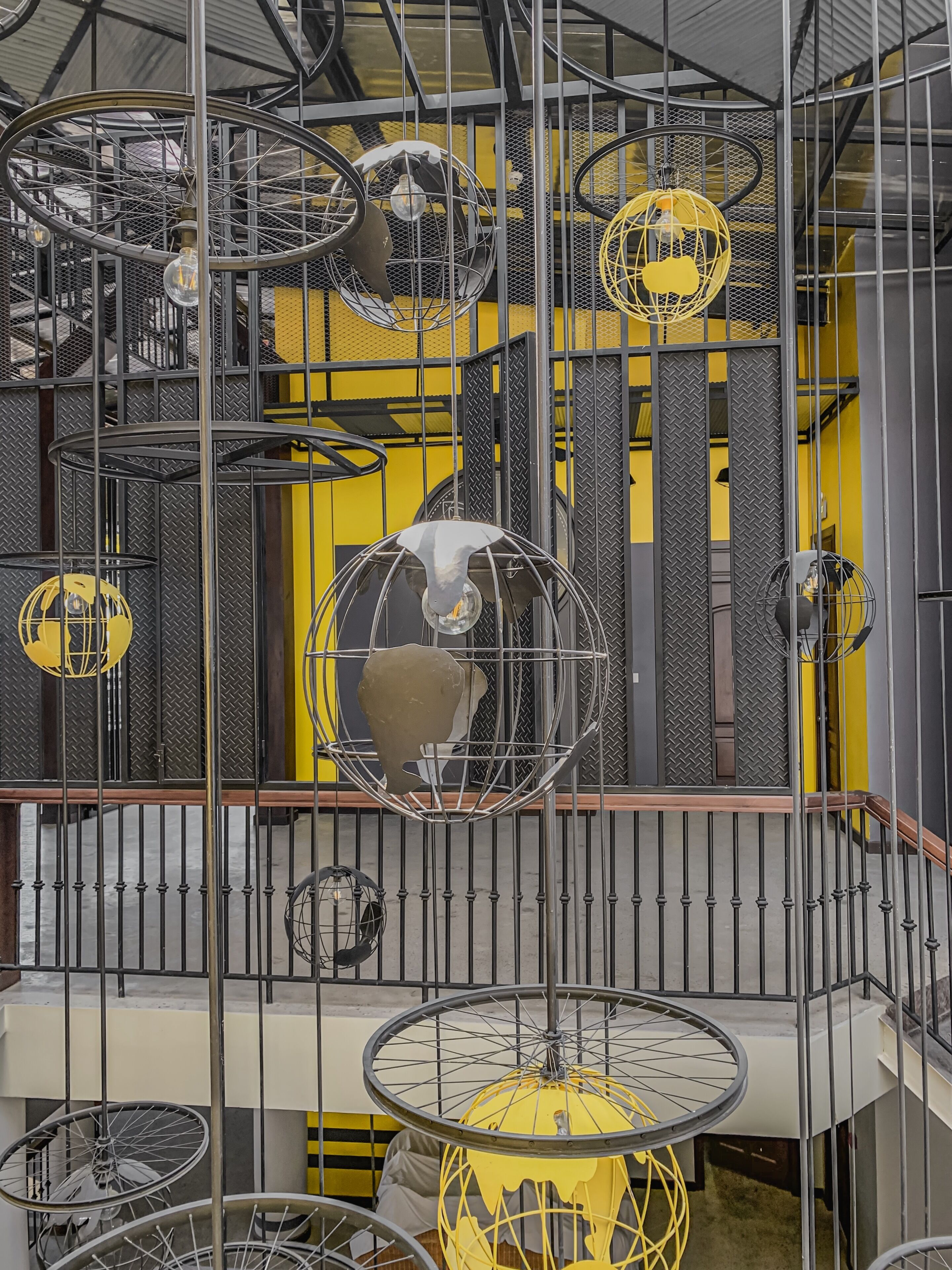 Un atrium à plusieurs niveaux, doté d’un design industriel moderne, avec des garde-corps en métal apparent et des luminaires sphériques suspendus.