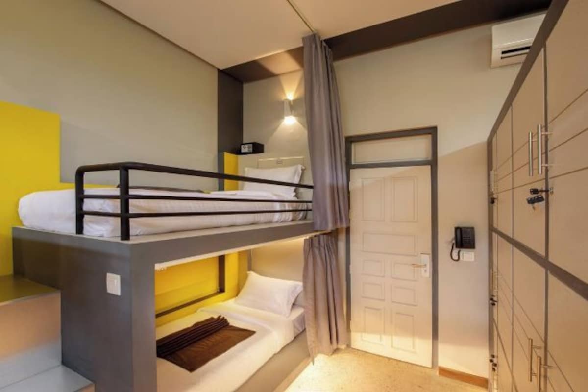 Une chambre avec un lit superposé, un bureau, un téléphone et une porte.