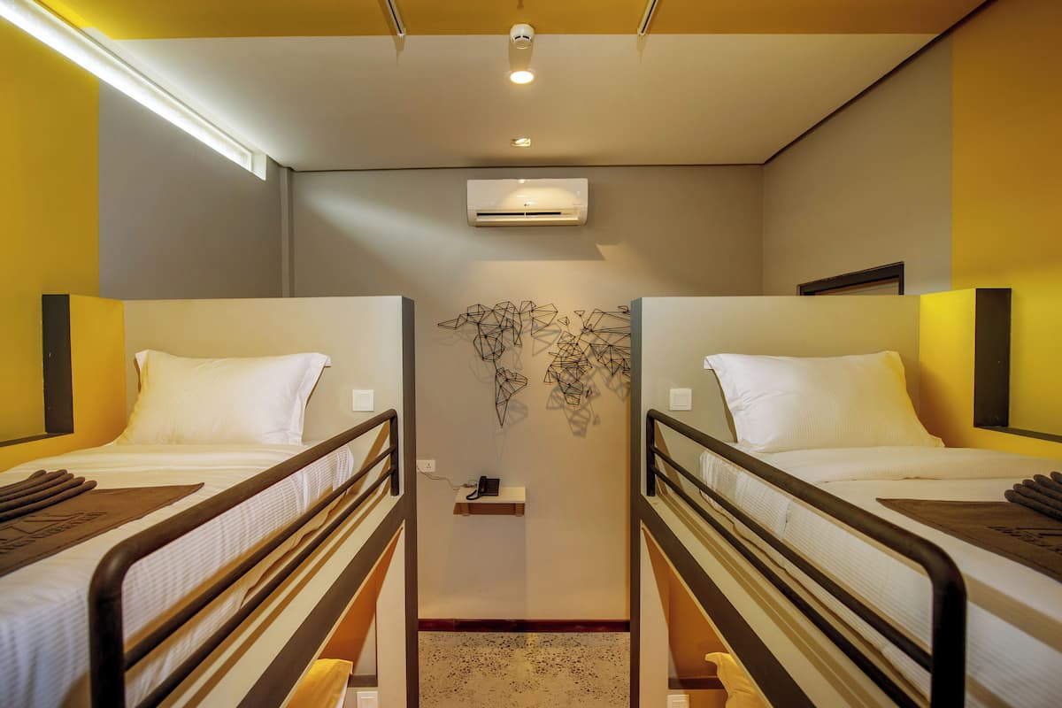 Une chambre d’hôtel avec deux lits simples, un climatiseur fixé au plafond et une œuvre d’art accrochée au mur.
