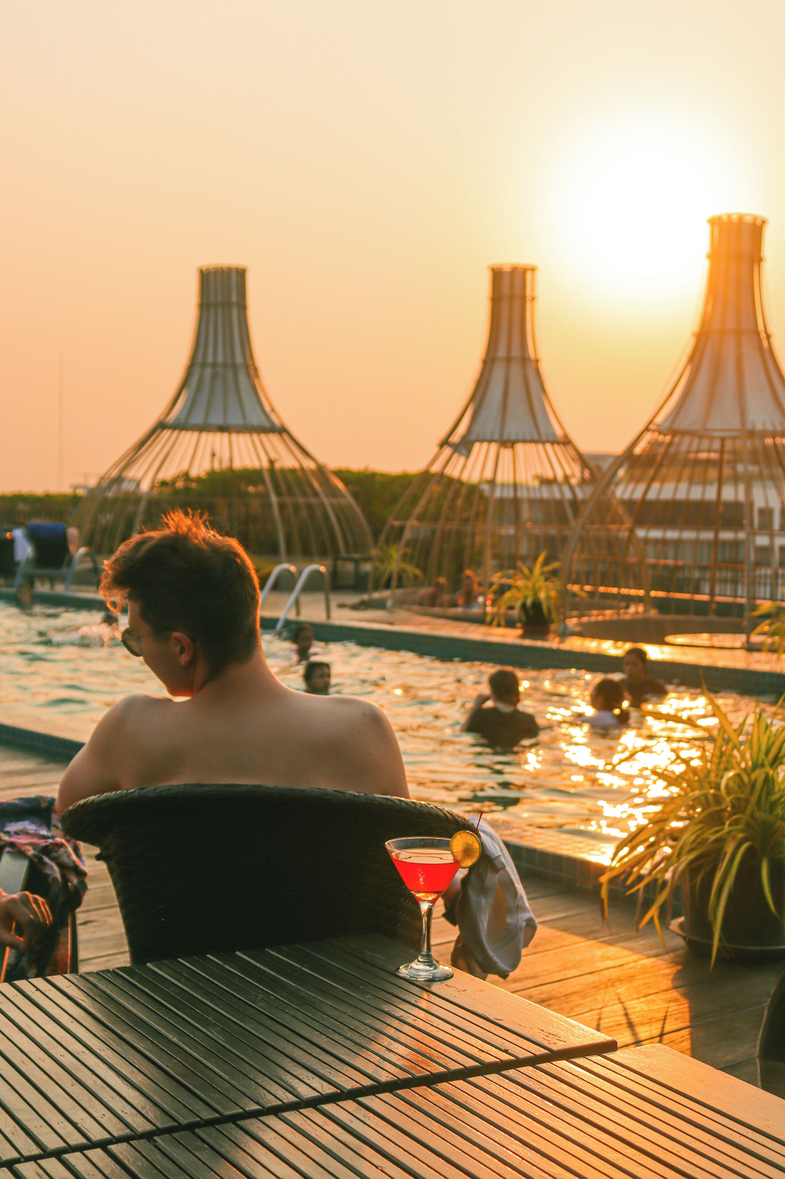 A poolside area with a table and a drink, surrounded by lounge chairs and umbrellas.