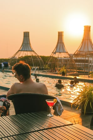 Zona de piscina con mesa, una bebida, sillas de descanso y sombrillas.