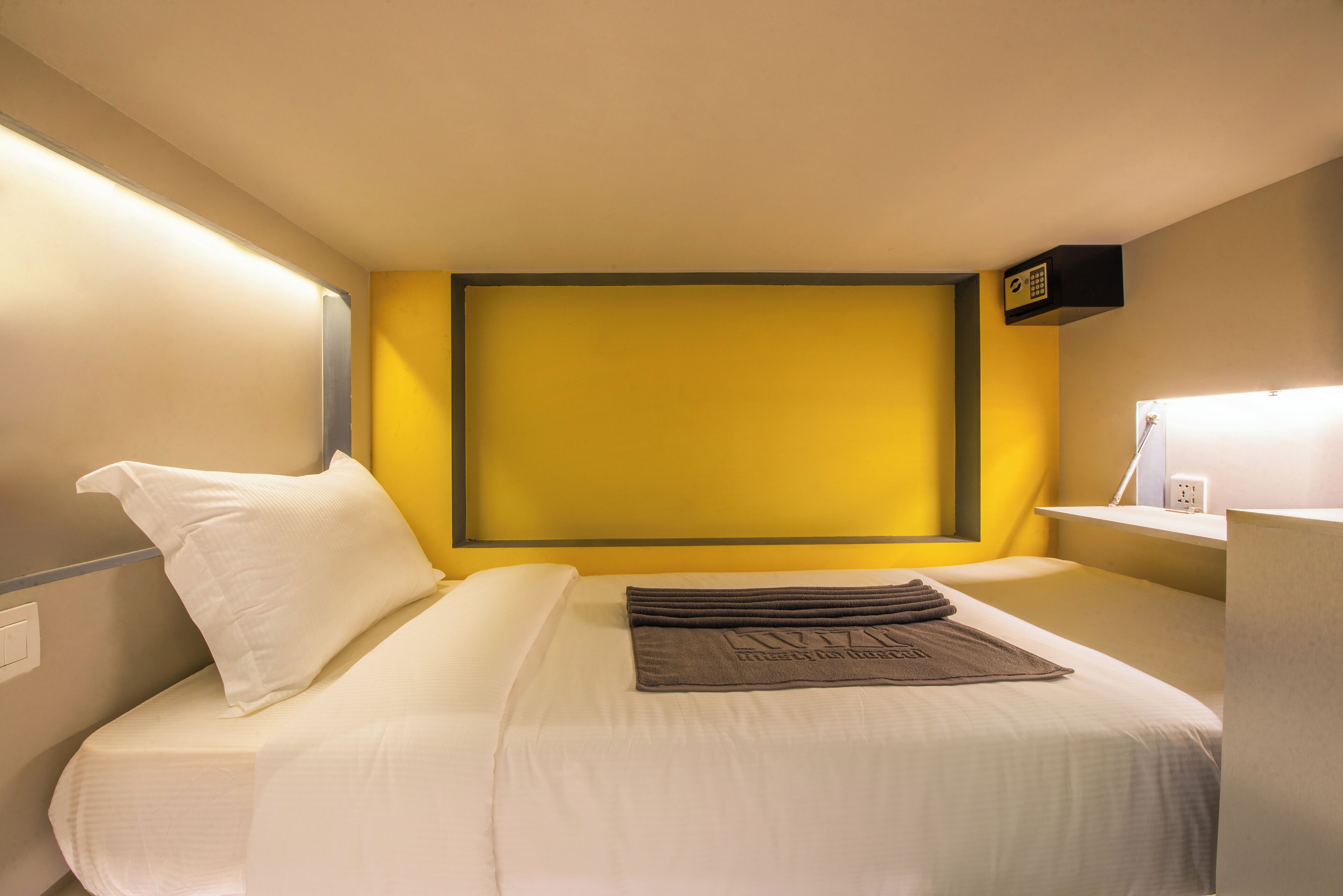 A hotel room with a bed, a bedside table, and a wall-mounted shelf with a lamp.