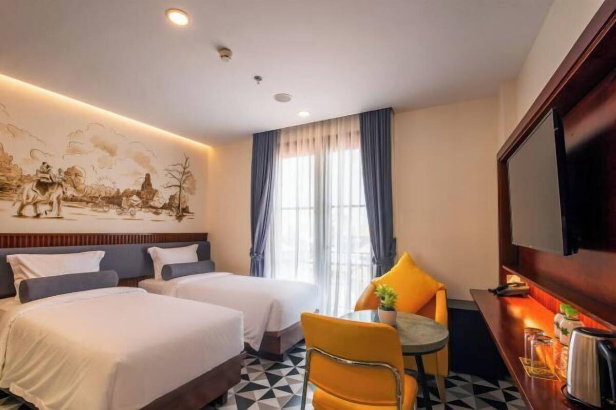 Une chambre d’hôtel avec deux lits, une table à manger, une chaise, un téléviseur et une fresque murale.