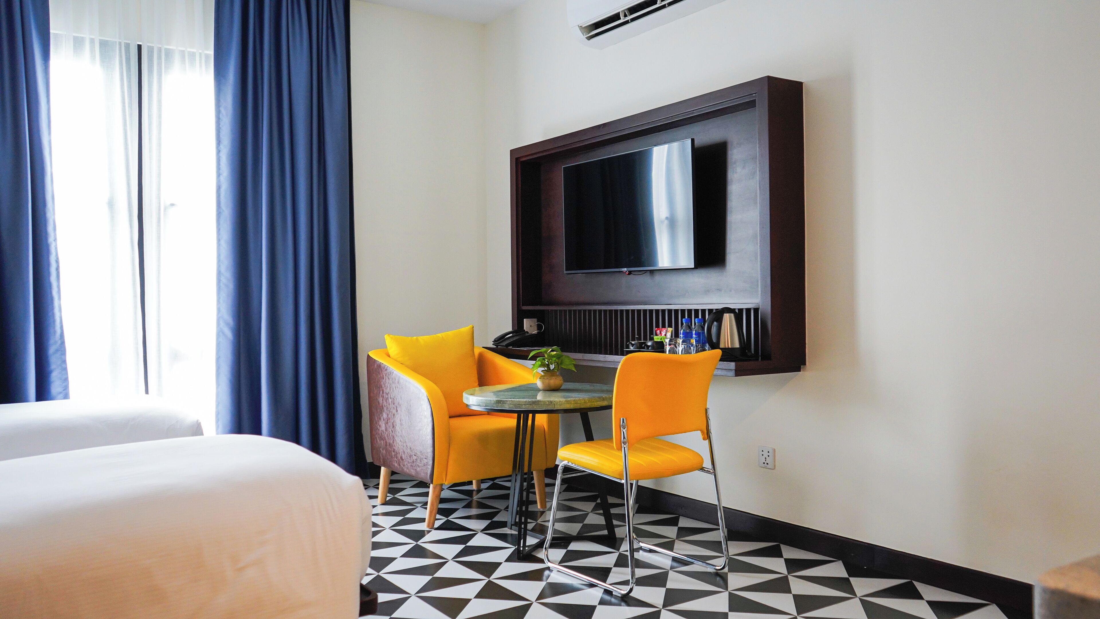 Une chambre d’hôtel avec un lit, une petite table ronde et deux chaises, un téléviseur à écran plat fixé au mur et un sol à motifs.