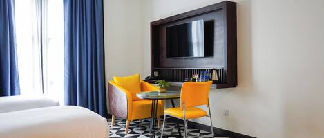 Une chambre d’hôtel avec un lit, une petite table ronde et deux chaises, un téléviseur à écran plat fixé au mur et un sol à motifs.