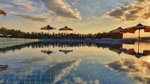 A swimming pool with clear blue water, surrounded by a tiled deck and umbrellas.