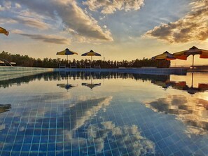 Una piscina al aire libre, sombrillas, sillones reclinables de piscina