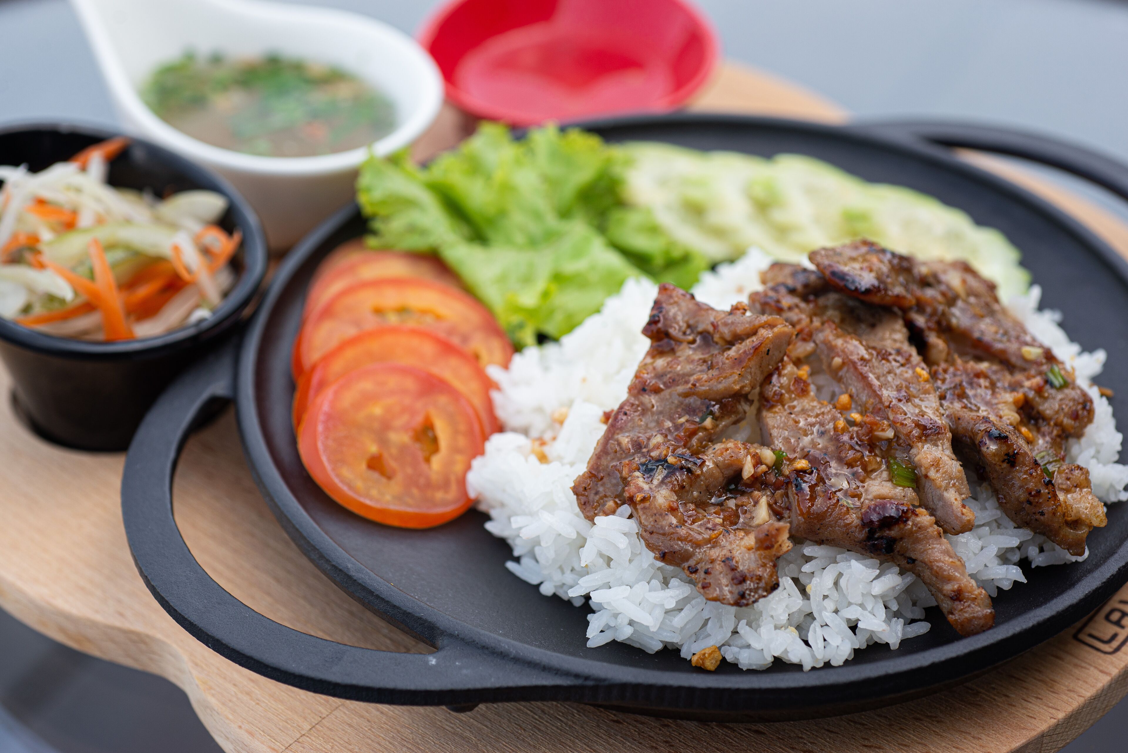 A plate with white rice, grilled meat, sliced tomatoes, lettuce, and a side of pickled vegetables.