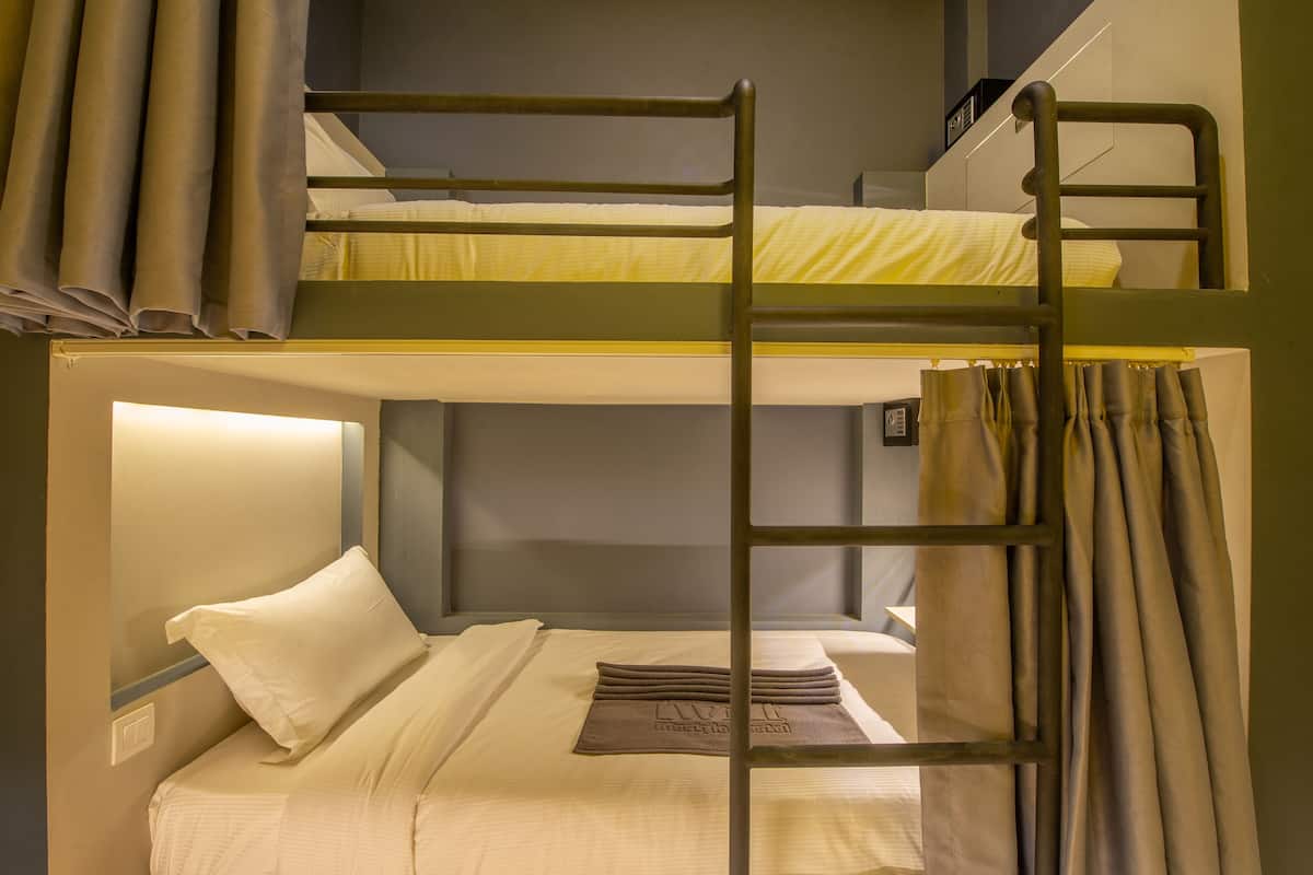 Une chambre avec un lit superposé, une échelle, des rideaux et un oreiller orné d’un logo.