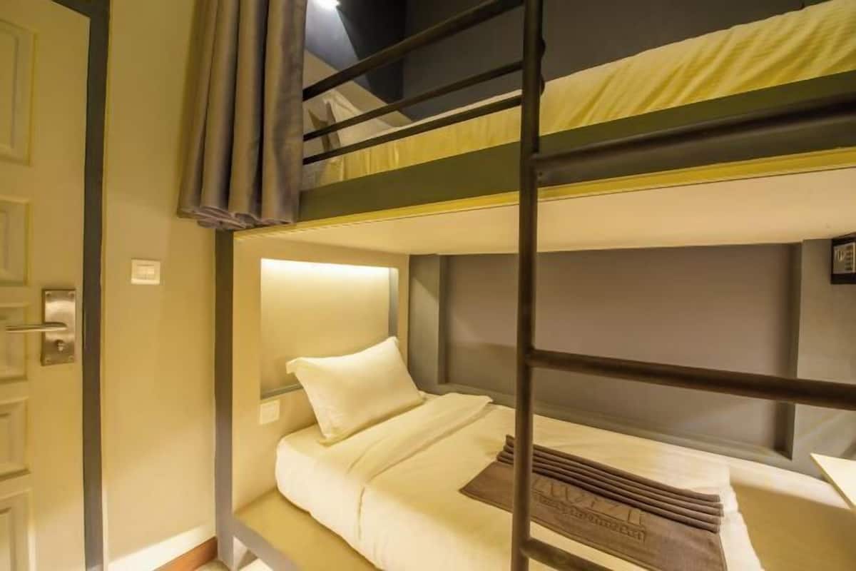 Une chambre avec un lit superposé, une porte, une table de chevet et une tête de lit.