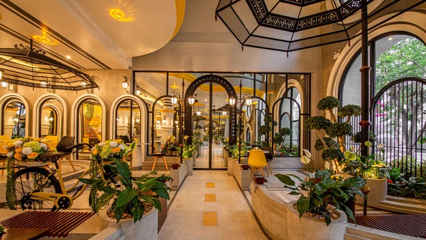 A hotel lobby with a central staircase, arched doorways, and potted plants.