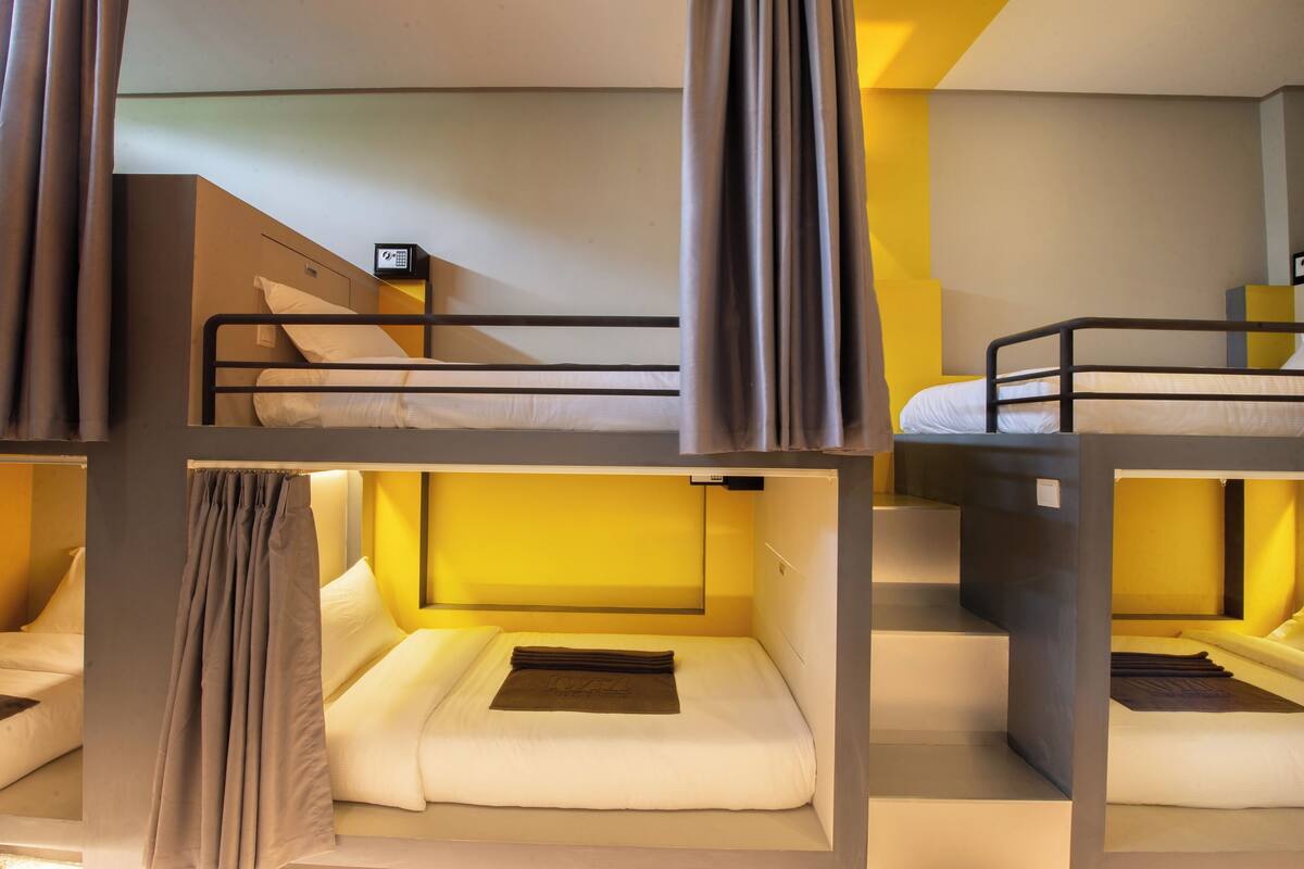 Une chambre avec un lit superposé, un panneau de commande, des rideaux et un lit avec une couverture.