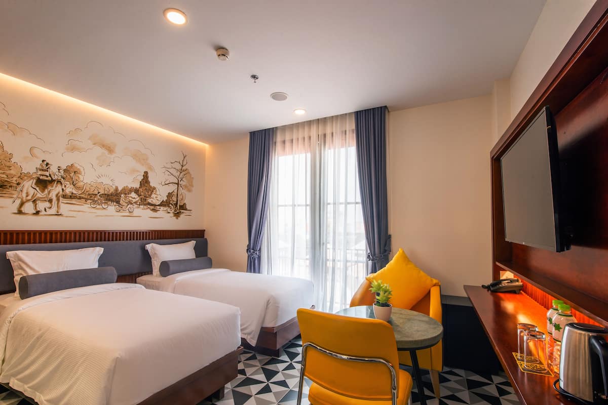 Une chambre d’hôtel avec deux lits, une table à manger avec une chaise, un téléviseur et une fresque murale.