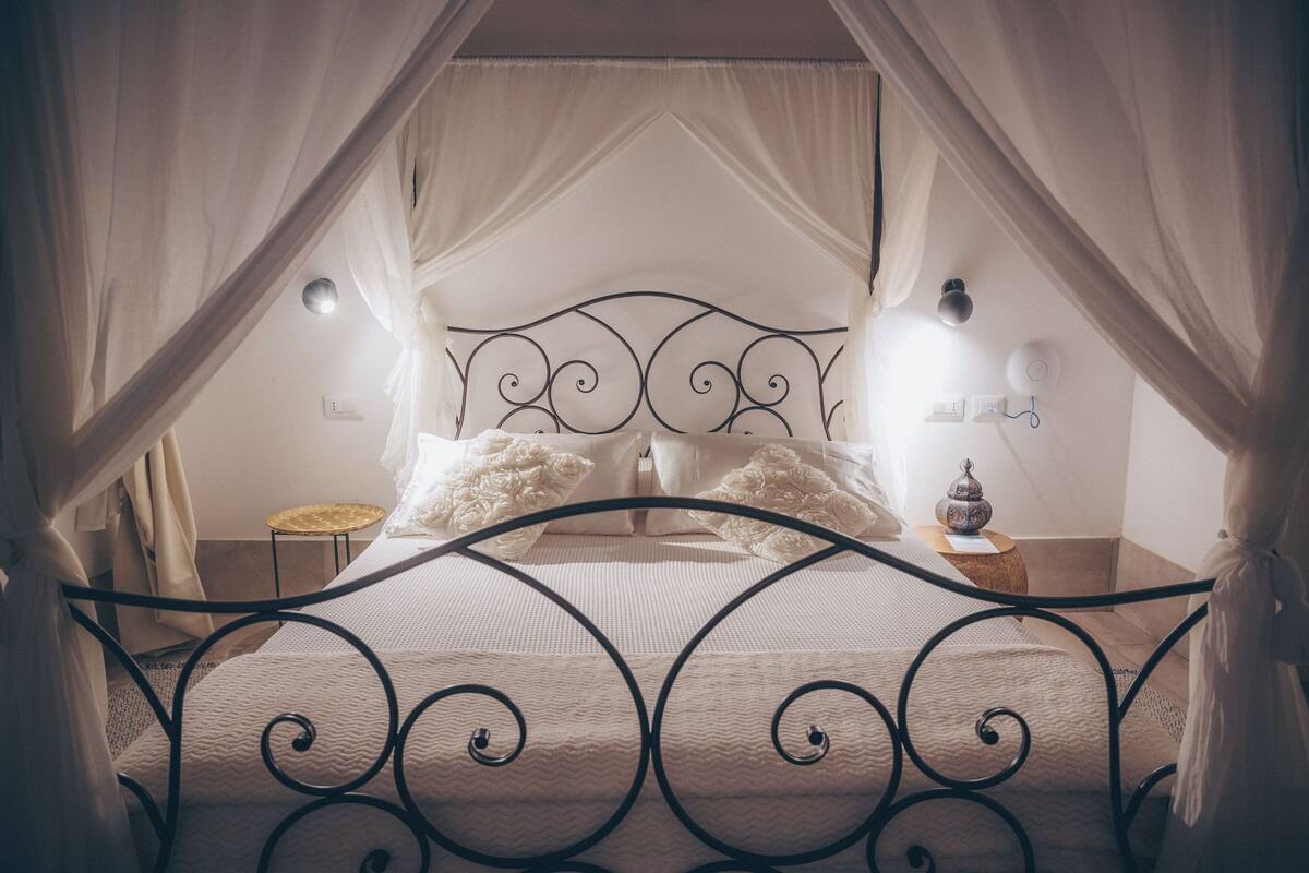 A bed with a canopy, a bedside table with a lamp, and a wall-mounted light fixture.
