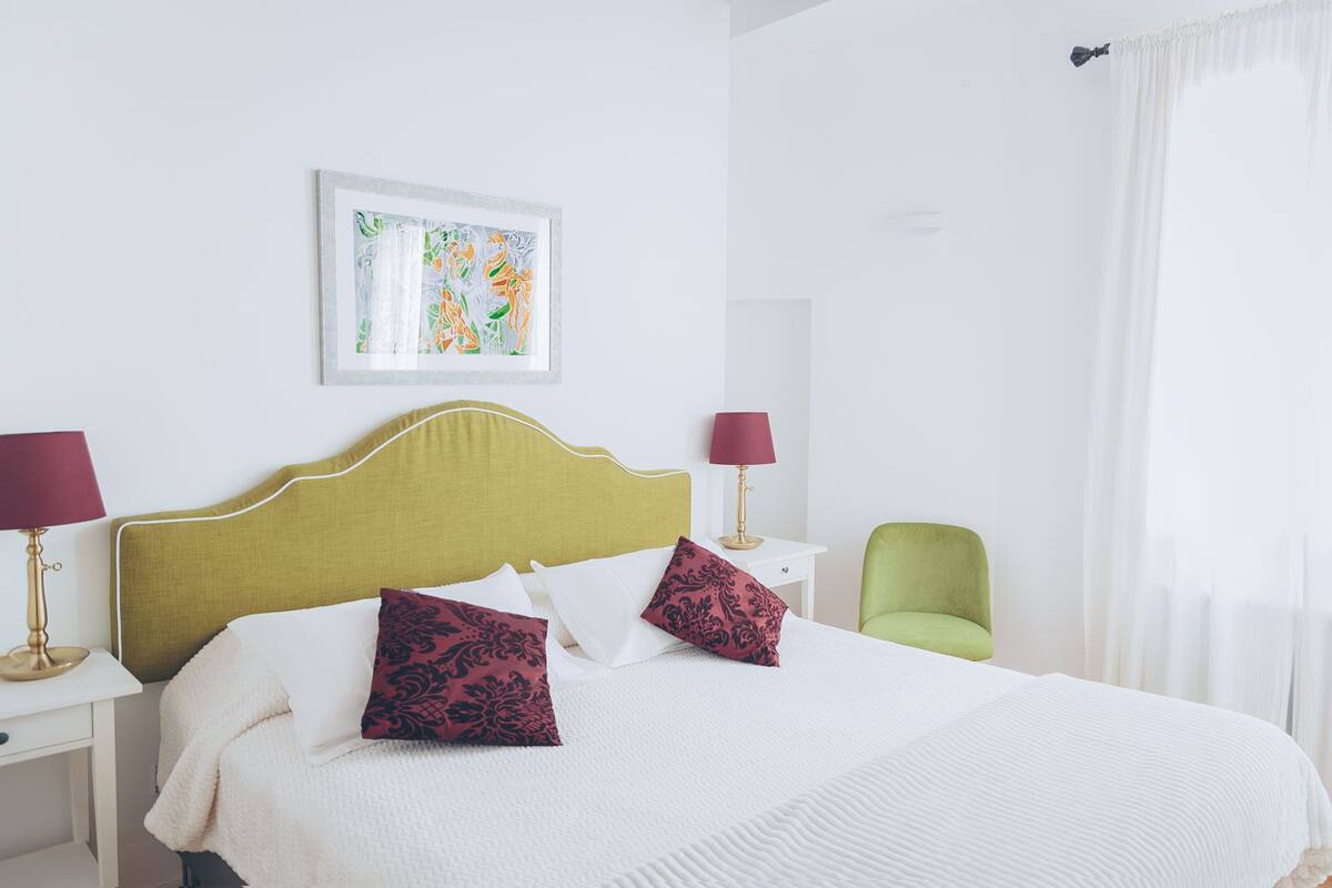 A neatly arranged hotel room with a bed, two bedside tables, a chair, and a painting on the wall.