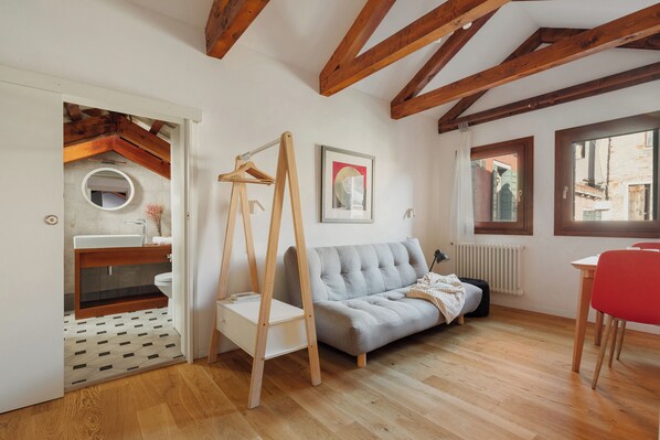 Una habitación con techo de madera, un sofá gris, una silla roja, una mesa blanca y una ventana con vistas.