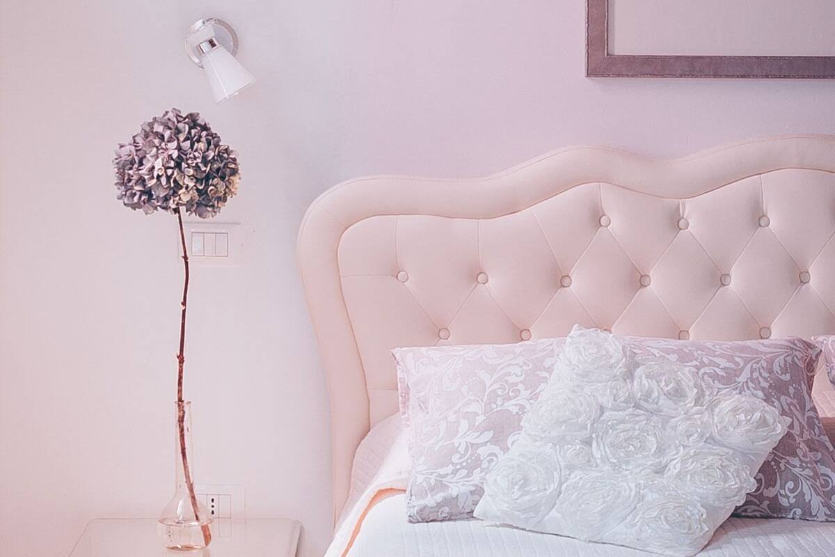 A bedroom with a tufted headboard, a glass bedside table with a vase, and a patterned bedspread.