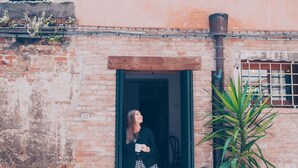 Una mujer parada frente a la entrada de un edificio de fachada de ladrillo y puerta de madera.