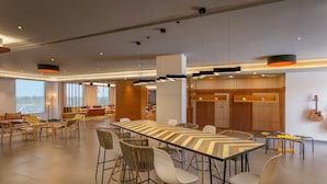 A spacious lounge area with a long table and multiple chairs, a wooden partition with slats, and a guitar on the wall. - Ginger Sanand (Sanand)