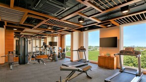 A gym with treadmills, exercise equipment, and large windows offering a view of greenery. - Ginger Sanand (Sanand)