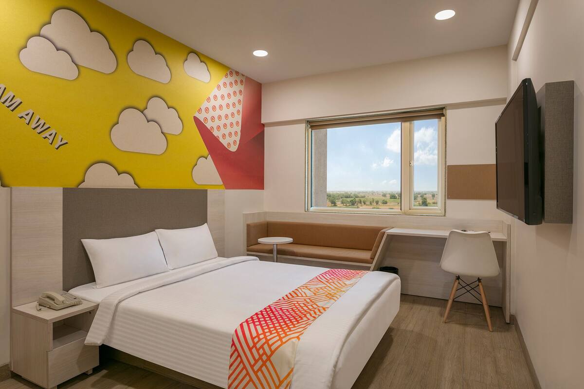 Quarto de hotel com uma cama, uma mesa pequena, um sofá, uma televisão e uma janela com vista.