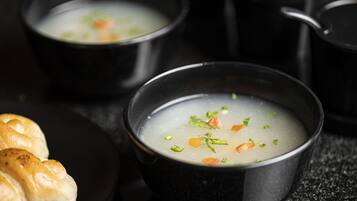 Tres tazones negros de sopa con vegetales, acompañados de un plato de pan.