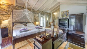 A bedroom with a stone wall, a canopy bed, a television, and a cabinet. - Beautiful stone holiday house MENTA I (Bajcici)