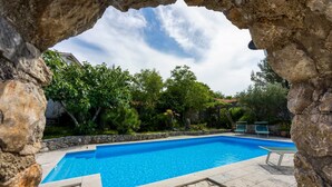A swimming pool with a stone border, surrounded by greenery and a stone wall. - Beautiful stone holiday house MENTA I (Bajcici)