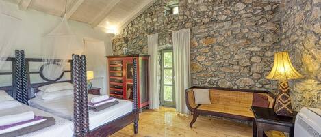 A bedroom with a stone wall, a bed with a canopy, a wooden chair, and a desk with a lamp.