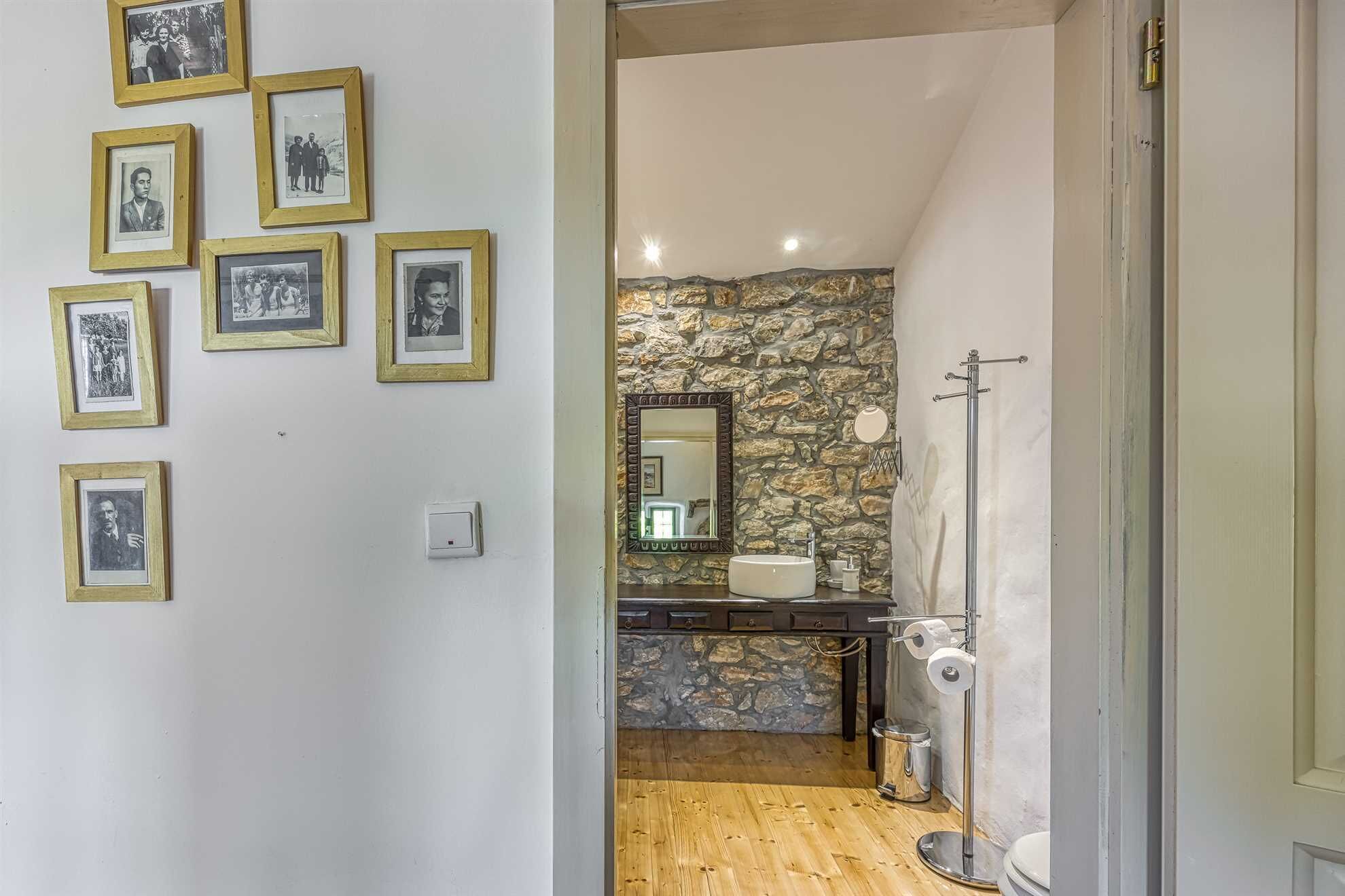 A bathroom with a stone wall, a sink, a mirror, and a toilet. There are framed pictures on the wall.