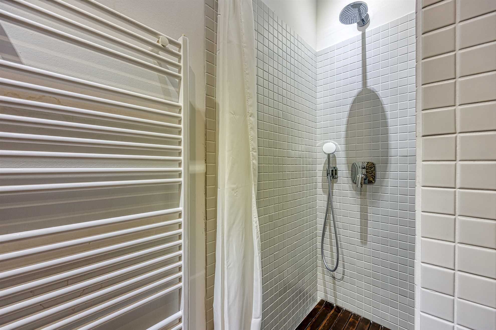 A bathroom with white tiled walls, a shower with a handheld showerhead, and a toilet with a wall-mounted bidet.