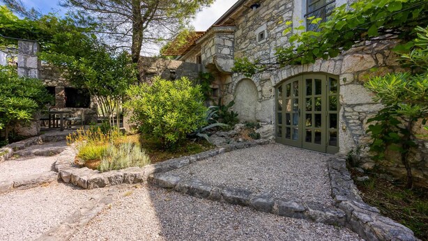 A stone building with a gravel courtyard, a wooden table and chairs, and a green door. - Beautiful stone holiday house MENTA I (Bajcici)