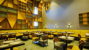A restaurant with yellow booths and tables, wooden shelves, and brick walls.