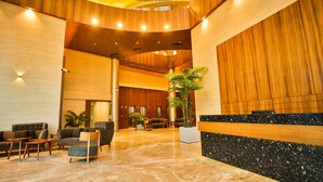 Een ruime lobby met een hoge plafond, houten lambrisering, een receptiebalie, zithoek en potplanten.