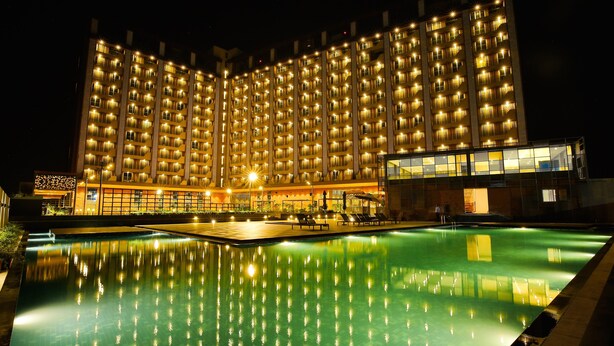 Een groot hotel met meerdere verdiepingen, een zwembad en een goed verlichte gevel.