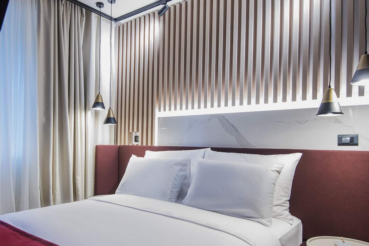 A modern hotel room with a large bed, a bedside table, and a wall-mounted light fixture.