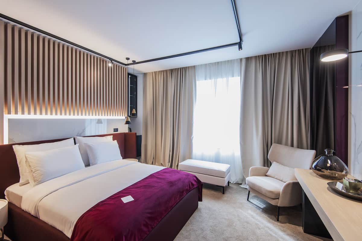 A modern hotel room with a large bed, a desk, and a chair.