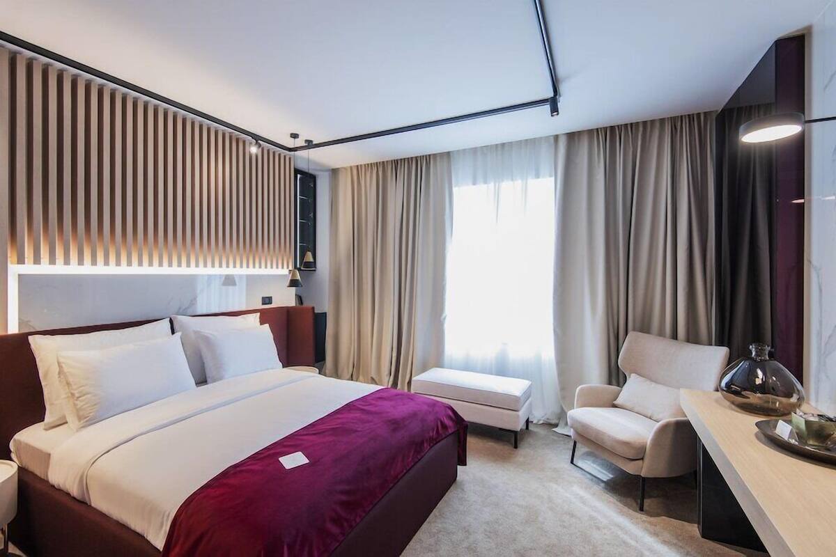 A modern hotel room with a large bed, a desk, a chair, and a view of the city.