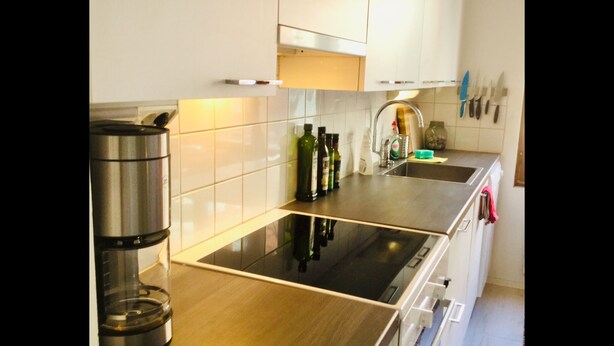 A modern kitchen with white cabinets, a stainless steel coffee maker, and a built-in oven. - Large artsy apartment in Pasila (Helsinki)