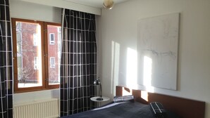 A bedroom with a large bed, a radiator, a lamp, and a window with curtains. - Large artsy apartment in Pasila (Helsinki)