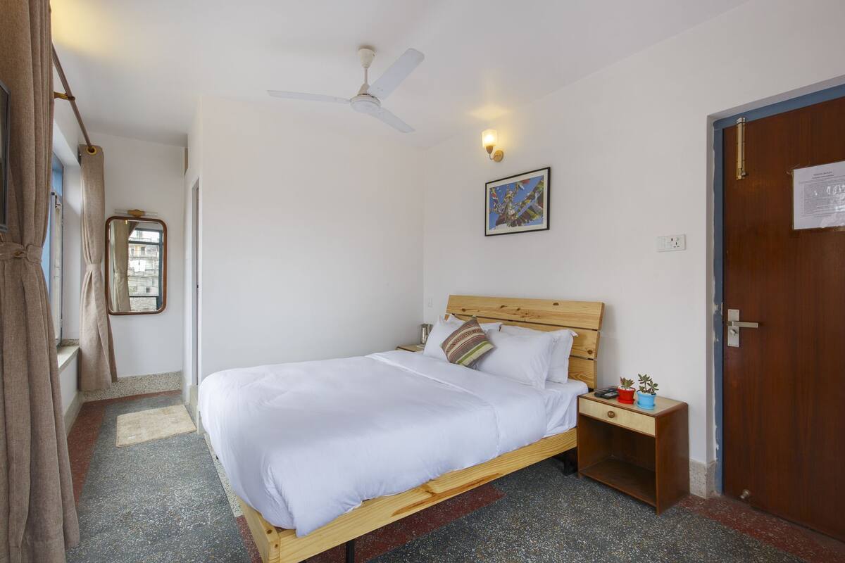 A single bed with a wooden headboard, a nightstand with a lamp, a ceiling fan, and a door with a sign.