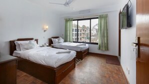 A hotel room with two beds, a ceiling fan, a TV mounted on the wall, and a window with curtains. - Pacific Guest House (Kathmandu)