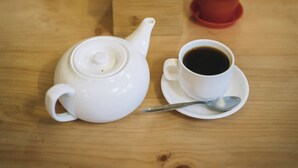 A wooden table with a white teapot, a cup of coffee, a small potted plant, and a tissue box. - Pacific Guest House (Kathmandu)