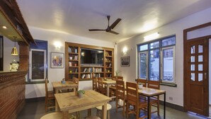 A dining area with wooden furniture, a ceiling fan, and a bookshelf. - Pacific Guest House (Kathmandu)
