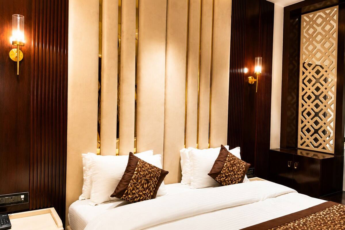 Habitación de hotel con una cama grande, dos apliques, un panel decorativo y un cabecero de madera.