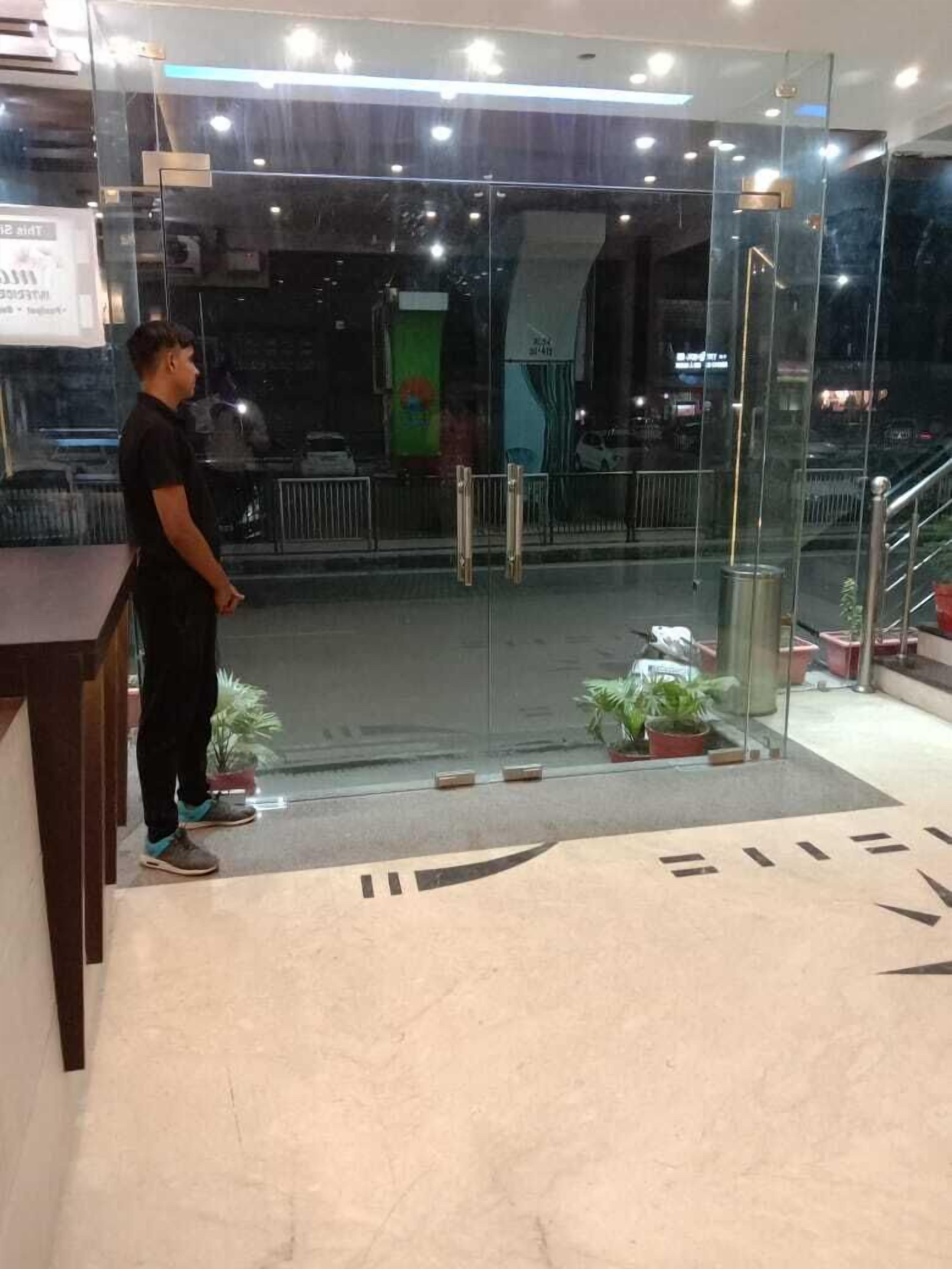 A modern hotel entrance with a glass door, potted plants, and a visible staircase.